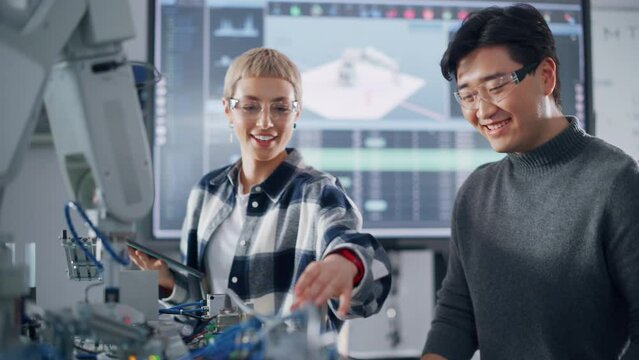 Positive Student Telling to her Asian Classmate while Analysing Work of Bionic Hand with Black Teacher at University. Diverse Group Programming Robotic Arm. Computer Science Concept. Slow Motion