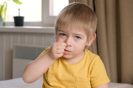 Child boy with blonde hair baby with finger in his nose. Portrait 3 years old kid picking his nose. Boy toddler at home. Early age children education development. Authentic candid lifestyle