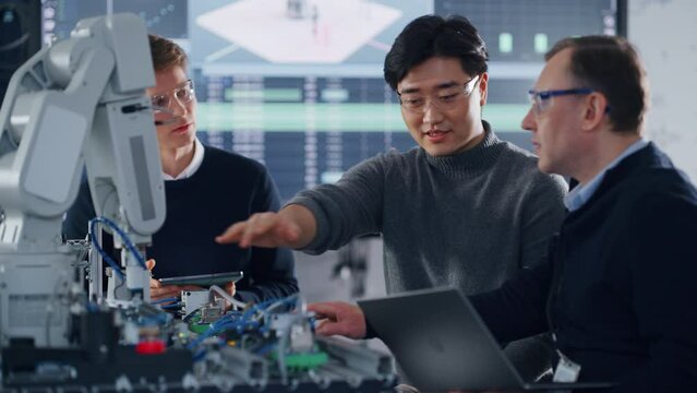 Students Advising with their Male Teacher while Working on Project with Robotic Arm. People with Tablet and Laptop at Hands. Modern Technologies, Science and Developing Concept