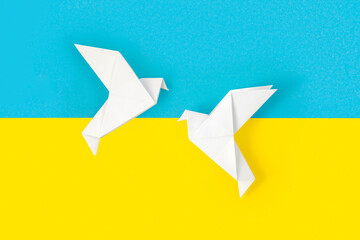 Two white origami paper doves on colors of flag of Ukraine. The concept of peace between two states. Symbol of peace on blue and yellow background. Independence. Stop war. Copy Space for text