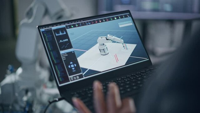 Black Female Developer Typing at Laptop Keyboard while Programming Bionic Claw. Robot is Moving Under her Control. Female Specialist in Robotics Facility Working on Software Production. Close Up View