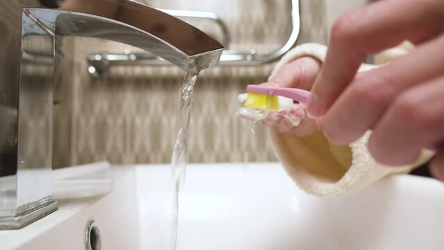 Close-up of unrecognizable caucasian young woman toothbrushing her kappa aligner under running water in bathroom sink. Care of dental accessories