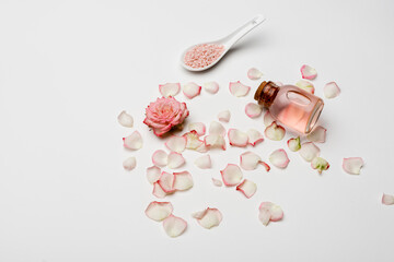 high angle view of rose near petals, pink sea salt and bottle with rose water on white.