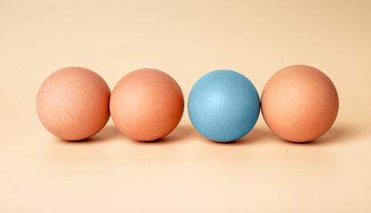 Outstanding blue dyed Easter egg among brown-shelled ones on beige background. Standing out from crowd, genius, difference concept. High quality photo
