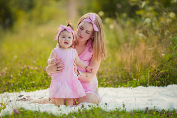 mother and daughter in pink dresses sit on a white blanket