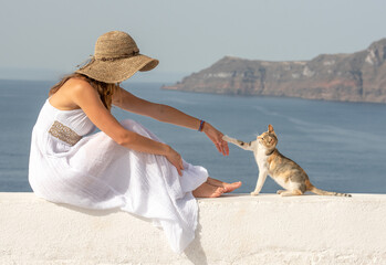 Young beautiful pretty woman in white dress with long hair sitting on white wall in Santorini greek...