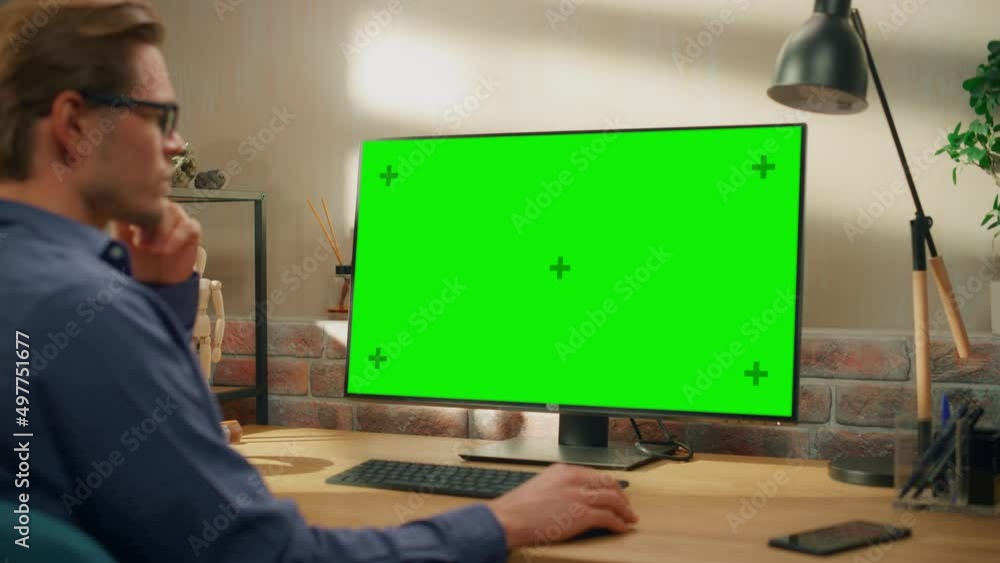 Poster Young Handsome Man Working from Home on Desktop Computer with Green Screen Mock Up Display. Creative Male Checking Social Media, Browsing Internet. Living Room in Bright Loft Apartment. Arc Shot.