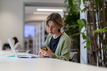 Pensive focused middle-aged woman university teacher using laptop while preparing materials for...