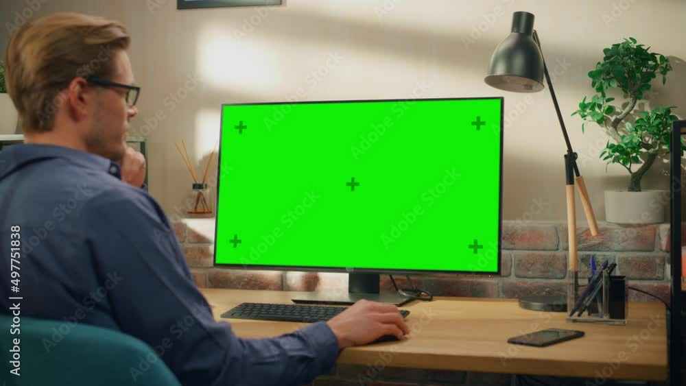 Poster Young Handsome Man Working from Home on Desktop Computer with Green Screen Mock Up Display. Creative Male Checking Social Media, Browsing Internet. Living Room in Bright Loft Apartment. Zoom In Shot.