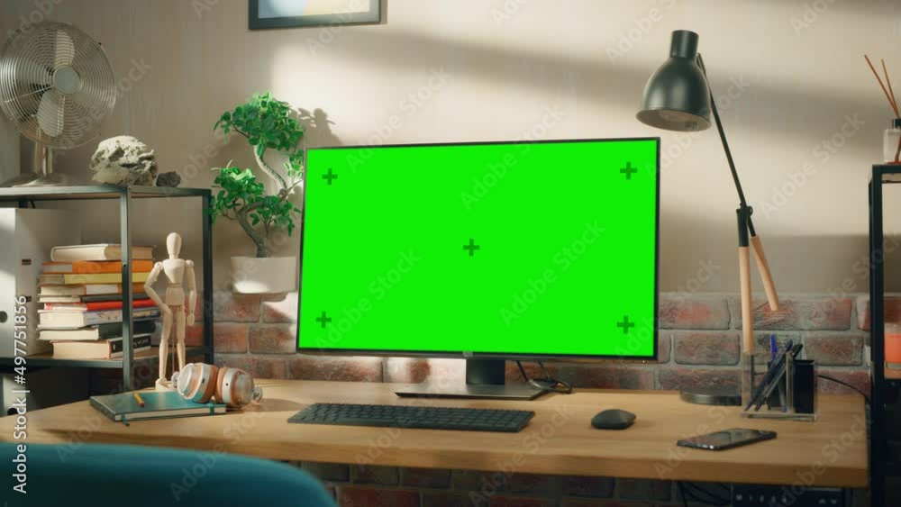 Poster Desktop Computer Monitor Standing on a Desk with a Green Screen Chromakey Mock Up Display. Cozy Empty Loft Apartment with a Lamp, Notebooks and Smartphone on the Table. Zoom In Shot.