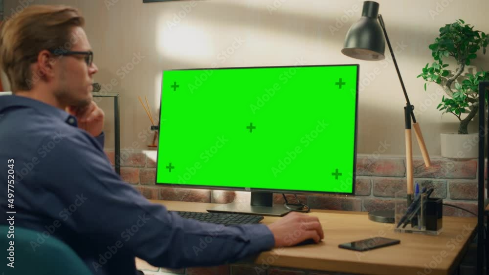 Poster Young Handsome Man Working from Home on Desktop Computer with Green Screen Mock Up Display. Creative Male Checking Social Media, Browsing Internet. Living Room in Bright Loft Apartment. Static Shot.