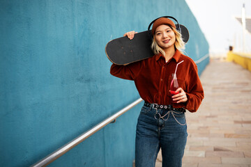 Portrait of fashion Asian woman with skateboard. Urban blonde woman listening the music while enjoy outside
