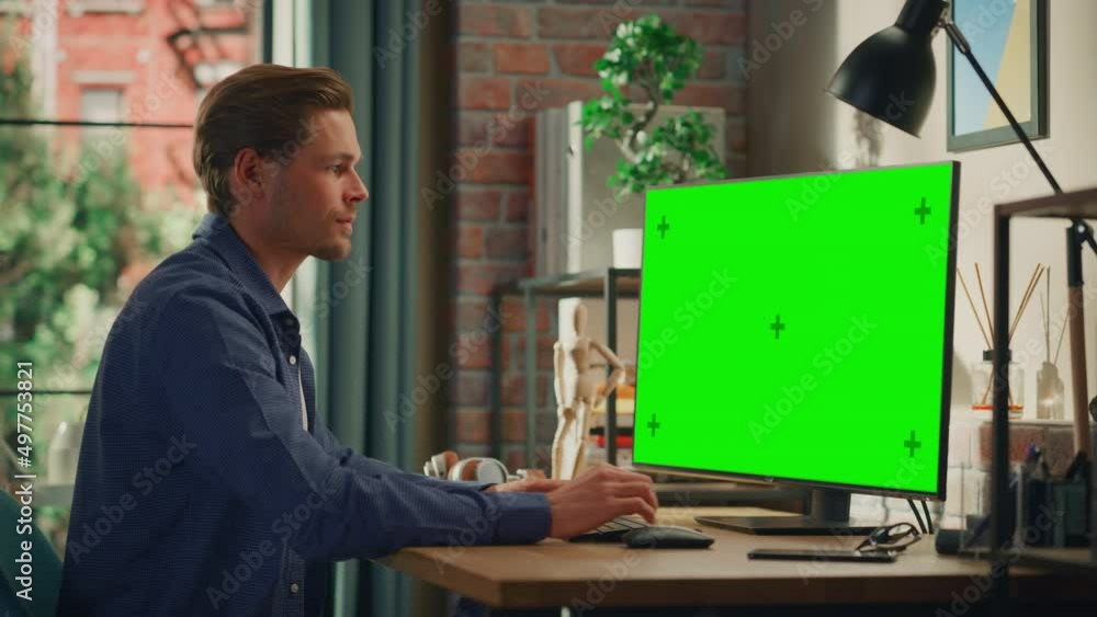 Poster young handsome man working from home on desktop computer with green screen mock up display. male che