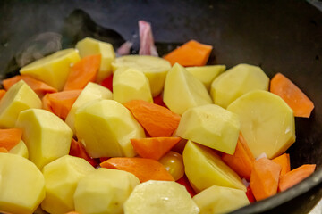 Carrots with potatoes and other vegetables are stewed on fire in a saucepan