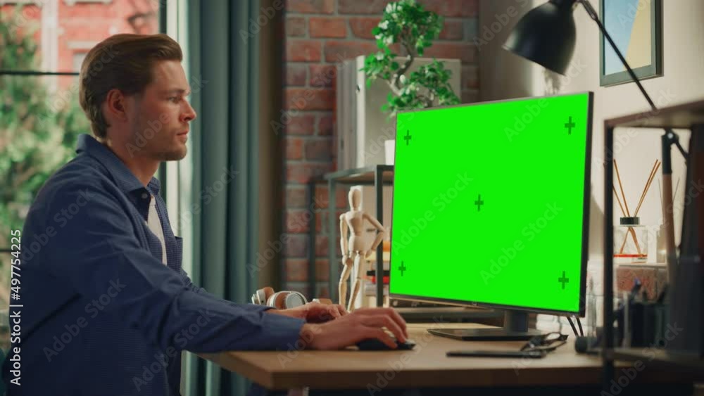 Poster young handsome man working from home on desktop computer with green screen mock up display. male che