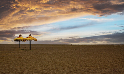 deserted empty tropical sand beach, two isolated tiki thatch umbrellas, storm clouds - early...