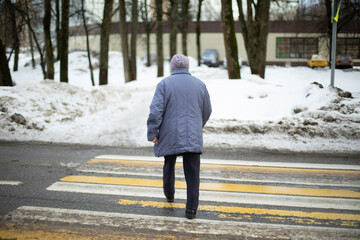 Woman crosses road on zebra. Pensioner in Russia walks down street.