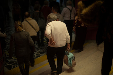 Fototapeta na wymiar People are walking inside building. Lot of people leave room. Old people after concert.