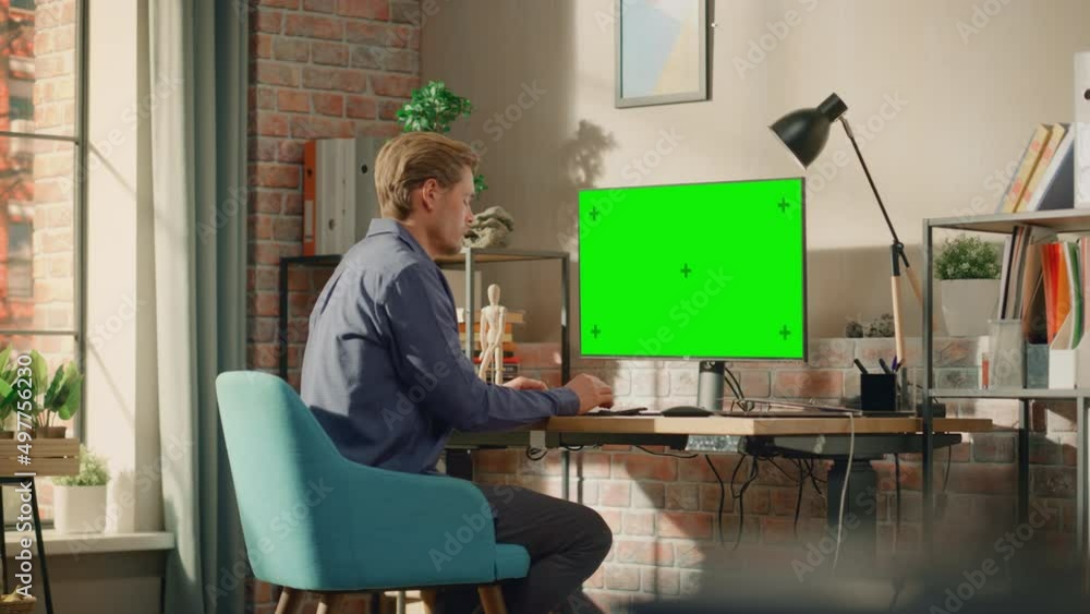 Poster Young Handsome Man Working from Home on Desktop Computer with Green Screen Mock Up Display. Creative Male Checking Social Media, Browsing Internet. Living Room in Bright Loft Apartment.