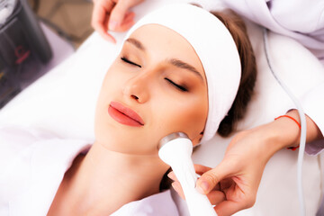 A woman receives ultrasonic cavitation of facial skin against aging. Phonophoresis or ultraphonophoresis apparatus in the hands of a beautician. Clinic of aesthetic cosmetology.