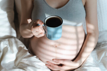 A pregnant woman holds a cup of coffee in her hands. Caffeine safety, myths about coffee during pregnancy concept 