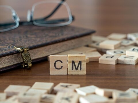 the acronym cm for contribution margin or dollar contribution per unit word or concept represented by wooden letter tiles on a wooden table with glasses and a book