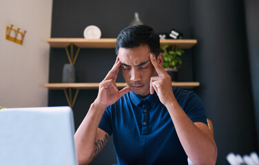 A young businessman rubs his temples at his desk, frowning