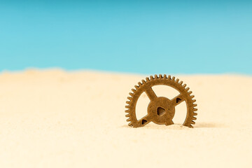 a metal gear, brass in the sand, a gear sticking out of the sand
