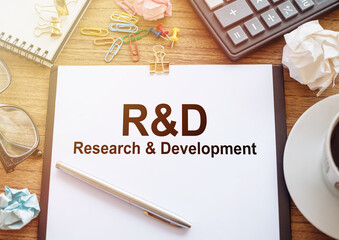 Glasses, pen, wrinkled paper, a cup of coffee, a calculator and a white sheet of paper with R and D Research and Developement on wooden background. Business and finance concept.