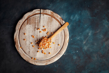 op view of corn grains in wooden spoon and  scattered grains on wooden plate over vintage surface background.