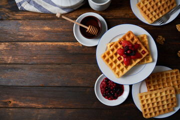 Breakfast waffles served with strawberries, blueberries, raspberries, honey, nuts on a wooden table. Top view.