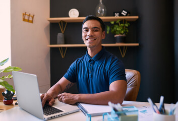 A young Asian man smiles at the camera in his office