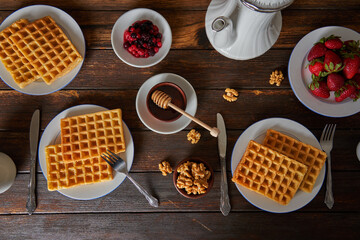 Breakfast waffles with strawberries, blueberries, raspberries, honey, nuts and a teapot on a wooden table.Top view.