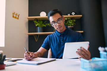 A young businessman takes notes from his digital tablet in a trendy office