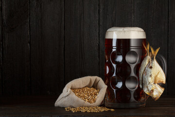 Fototapeta na wymiar Craft beer glass with dried salty fish snack and bag of barley grain for brewing