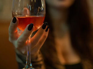 Unrecognizable woman holding a rose wine glass enjoying nightlife. Hand with black nails on a date...