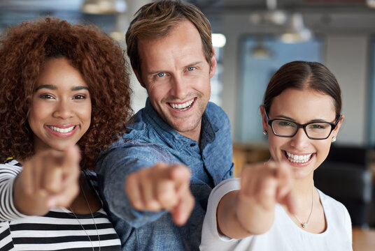 Were Confident About You. Three Friendly People Pointing At You With Their Office Space Behind Them.