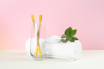 Bamboo toothbrushes, towel and bowl of baking soda on beige table against pink background