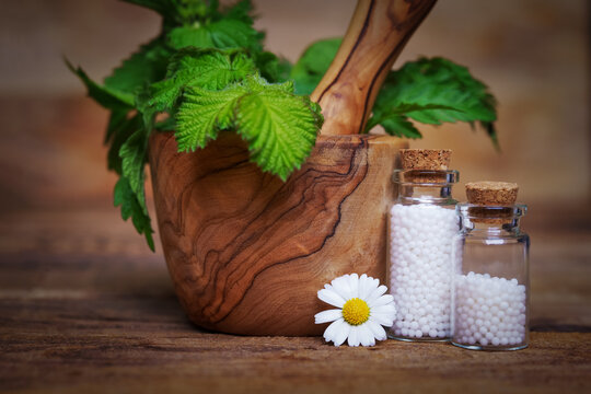 Bottles of globuli in front of a mortar with fresh green leaveson the wooden table. Homeopathic remedies.