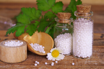 Medical glas vials and bowls on wooden table table, filled with globulis. Decoratet with fresh green leaves.