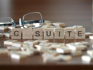 c suite word or concept represented by wooden letter tiles on a wooden table with glasses and a book