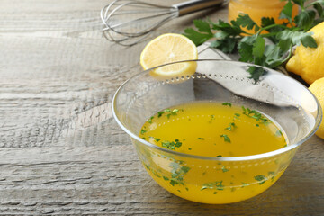 Bowl with lemon sauce and ingredients on wooden table, space for text. Delicious salad dressing