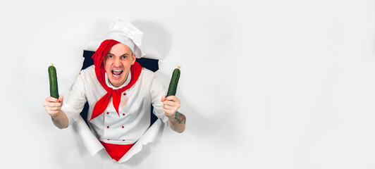 Young insane man dressed as chef with cucumbers. Crazy male cook with vegetables sticking out of hole of white background.