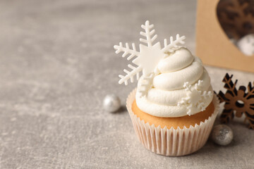 Tasty Christmas cupcake with snowflakes and festive decor on grey table. Space for text