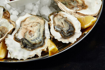 Oysters with lemon served on black round platter. Luxury delicatessen seafood.