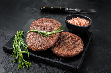 Beef burger patty cutlet for hamburger grilled on BBQ on marble board with rosemary. Black...