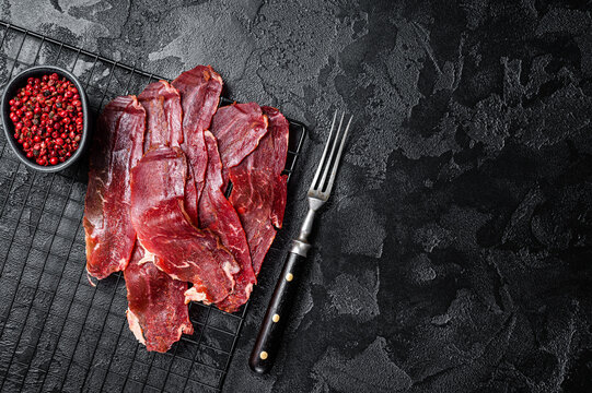 Dried sliced basturma, cured beef meat ready for eat. Black background. Top view. Copy space