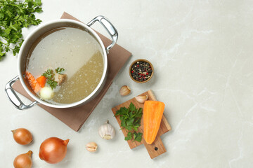 Pot with delicious bone broth and ingredients on light grey table, flat lay. Space for text