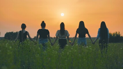 Girls stand holding hands at sunset on a summer evening.