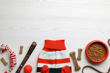 Flat lay composition with dog clothes, food and accessories on white wooden table. Space for text